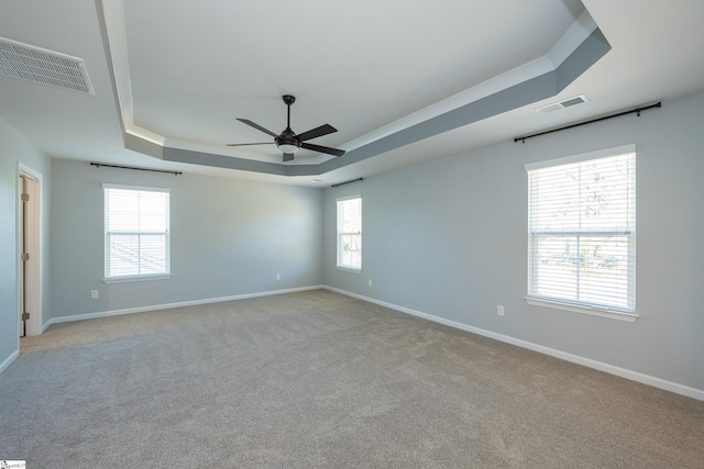 spare room with a tray ceiling, visible vents, and baseboards