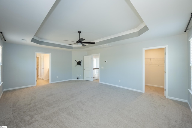 unfurnished bedroom featuring light carpet, baseboards, a tray ceiling, and a walk in closet