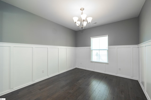 empty room featuring a wainscoted wall, dark wood finished floors, visible vents, and a notable chandelier