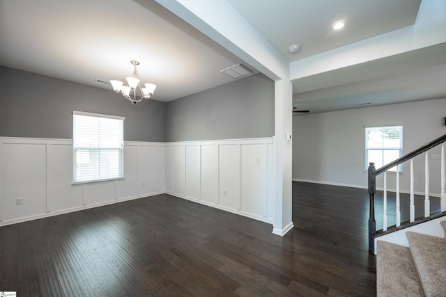 empty room featuring dark wood-type flooring, a wealth of natural light, stairway, and an inviting chandelier