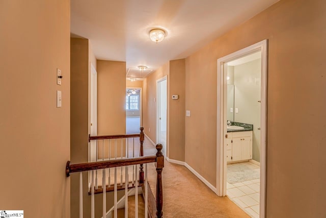 hallway featuring light carpet, a sink, an upstairs landing, and baseboards