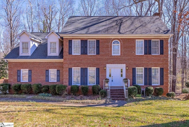 view of front of house with a shingled roof, a front yard, and brick siding