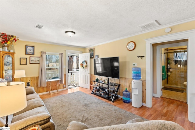 living area with a wainscoted wall, a textured ceiling, wood finished floors, and visible vents