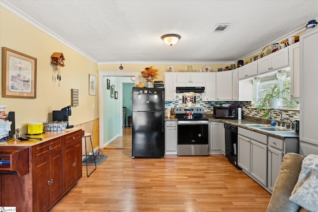 kitchen with light wood finished floors, ventilation hood, a textured ceiling, black appliances, and a sink