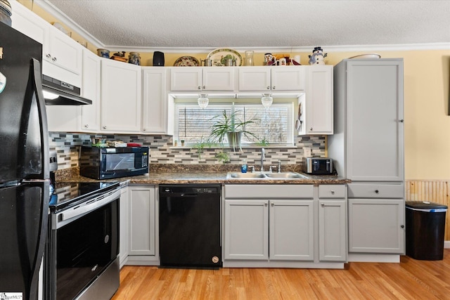 kitchen with light wood finished floors, a sink, a textured ceiling, under cabinet range hood, and black appliances