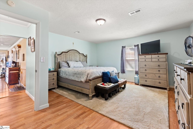 bedroom with baseboards, visible vents, a textured ceiling, and light wood finished floors