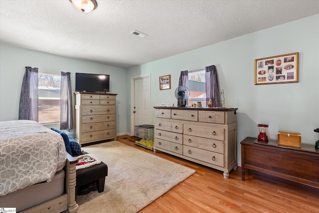 bedroom featuring a textured ceiling, multiple windows, visible vents, and wood finished floors