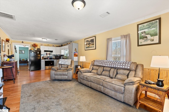 living room with ornamental molding, wainscoting, visible vents, and light wood finished floors