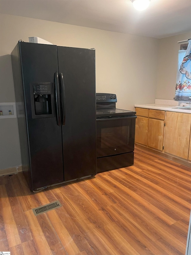 kitchen with visible vents, light countertops, brown cabinets, black appliances, and light wood finished floors