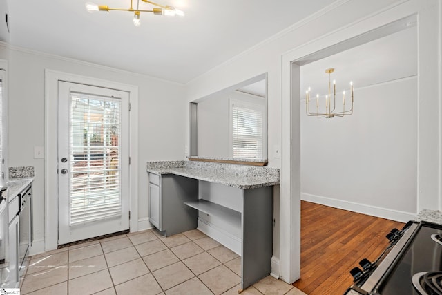 kitchen with light tile patterned floors, an inviting chandelier, ornamental molding, light stone countertops, and range