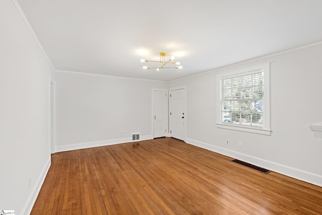 empty room with baseboards, visible vents, ornamental molding, wood finished floors, and a chandelier