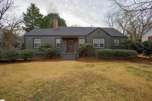 view of front of home with roof with shingles, a front lawn, a chimney, and board and batten siding