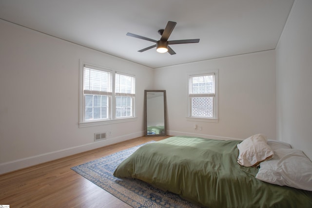 bedroom with multiple windows, wood finished floors, visible vents, and baseboards