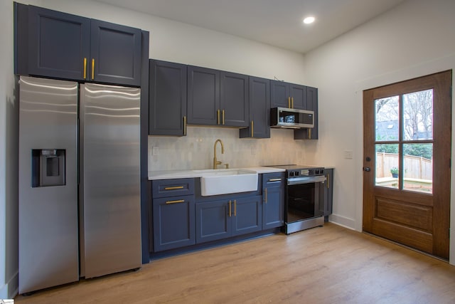 kitchen with light countertops, backsplash, appliances with stainless steel finishes, a sink, and blue cabinets