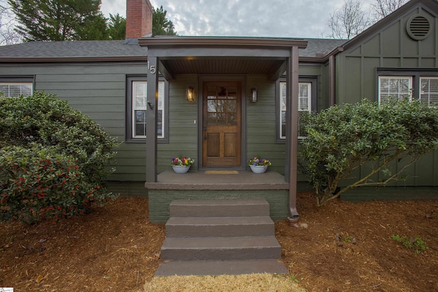 doorway to property with roof with shingles, board and batten siding, and a chimney