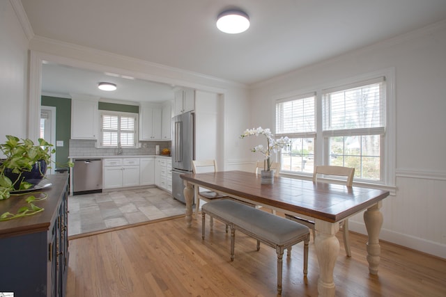 dining space featuring light wood-style floors, wainscoting, and crown molding