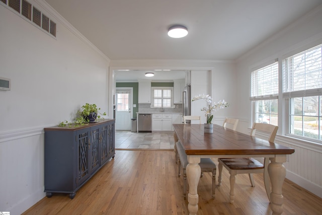 dining room featuring wainscoting, ornamental molding, light wood-type flooring, and visible vents