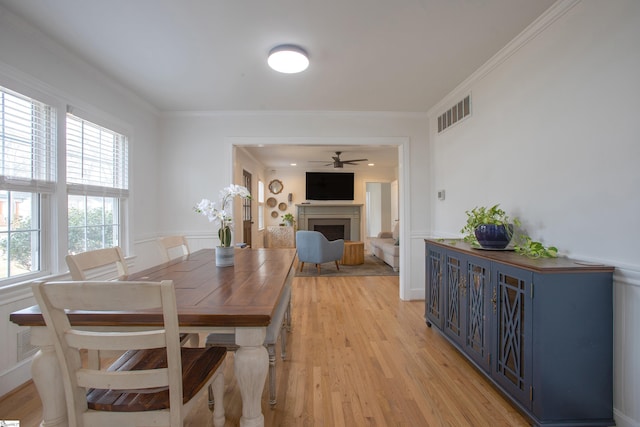 dining area featuring light wood-style flooring, a fireplace, visible vents, a ceiling fan, and ornamental molding