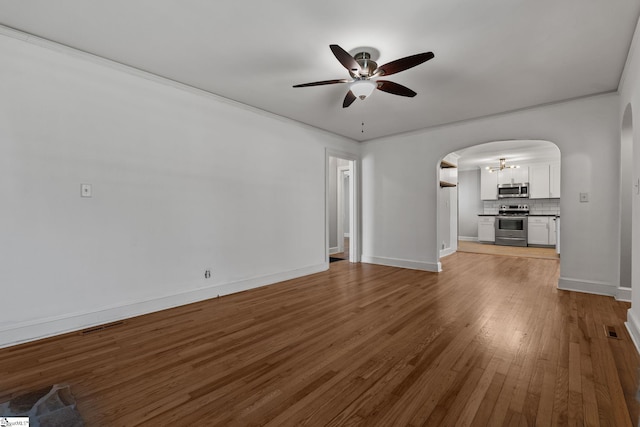 unfurnished living room featuring arched walkways, ceiling fan, wood-type flooring, and baseboards