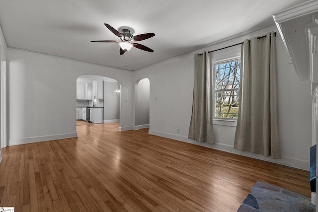 unfurnished living room with arched walkways, ceiling fan, light wood-style flooring, and baseboards