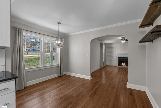 unfurnished dining area with a lit fireplace, arched walkways, dark wood-style flooring, and ornamental molding