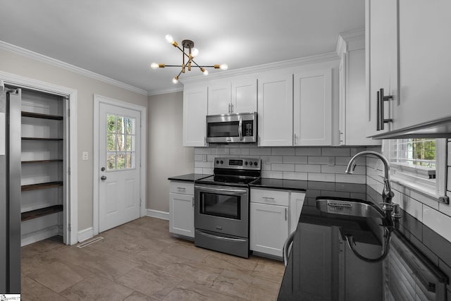 kitchen featuring stainless steel appliances, a sink, ornamental molding, dark countertops, and an inviting chandelier