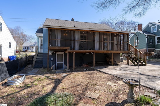 rear view of house with a sunroom, roof with shingles, and stairs