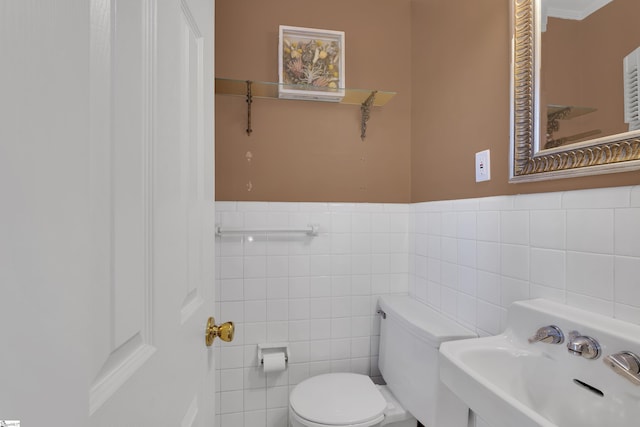 bathroom featuring wainscoting, a sink, toilet, and tile walls