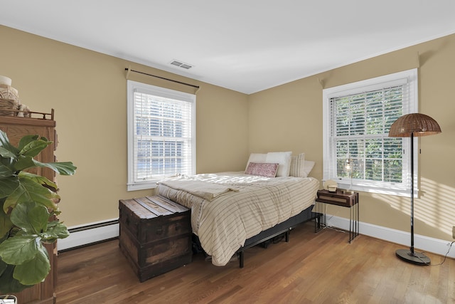 bedroom with baseboards, visible vents, a baseboard heating unit, and wood finished floors