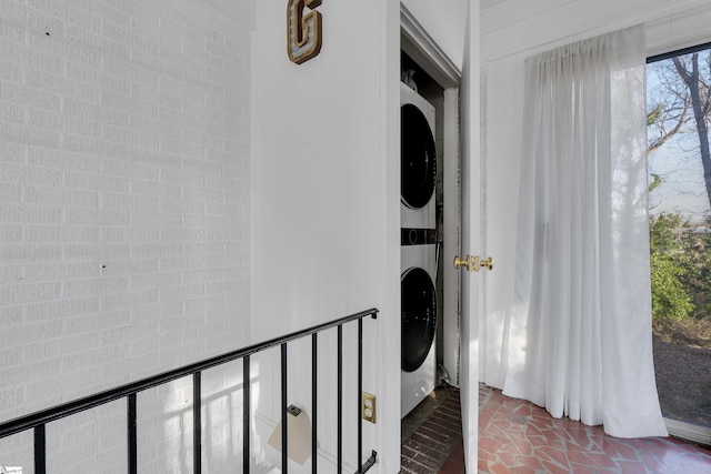 interior space featuring brick floor, brick wall, and stacked washing maching and dryer