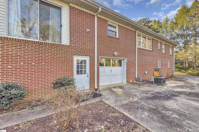 view of side of property featuring a garage, concrete driveway, brick siding, and central AC unit