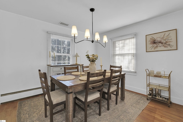 dining area with a baseboard heating unit, visible vents, crown molding, and wood finished floors