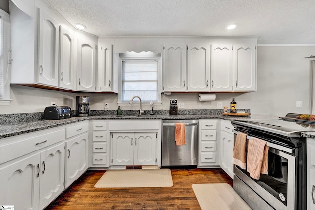 kitchen with dark wood-style floors, appliances with stainless steel finishes, white cabinets, a sink, and dark stone countertops