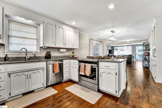 kitchen with appliances with stainless steel finishes, open floor plan, dark wood-type flooring, a peninsula, and a sink