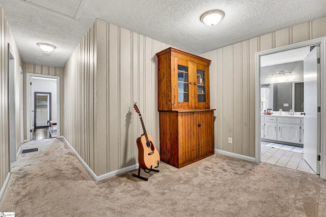 hallway with carpet, visible vents, a sink, a textured ceiling, and baseboards