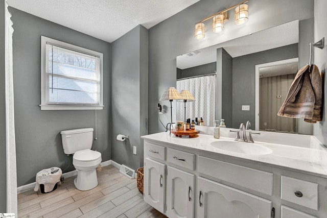 bathroom featuring toilet, vanity, a textured ceiling, wood finished floors, and baseboards