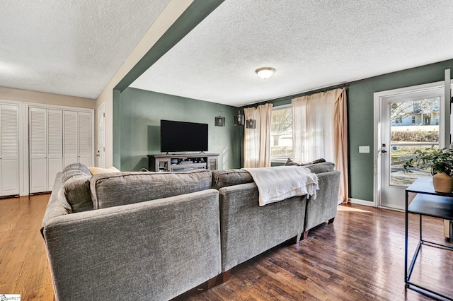 living area featuring a wealth of natural light, dark wood-style flooring, a textured ceiling, and baseboards