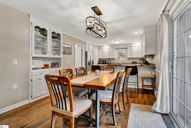 dining space with dark wood-style flooring, a notable chandelier, a textured ceiling, and baseboards