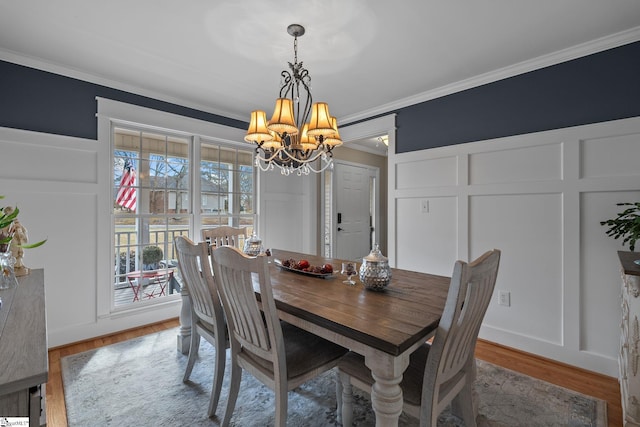 dining area featuring ornamental molding, an inviting chandelier, wood finished floors, and a decorative wall