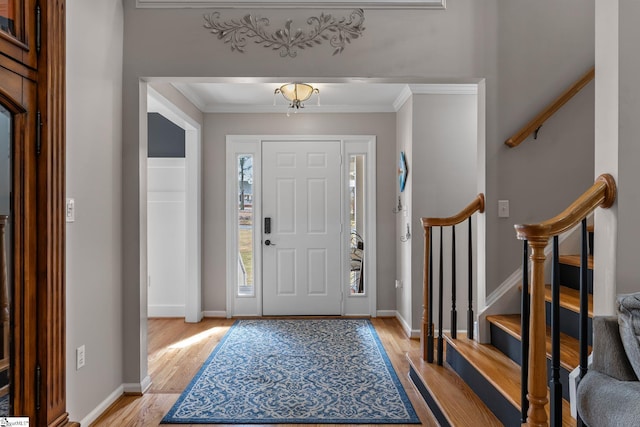 foyer with light wood-type flooring, stairs, baseboards, and crown molding