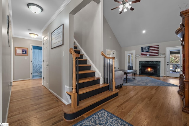 stairs with ceiling fan, a premium fireplace, wood finished floors, baseboards, and crown molding