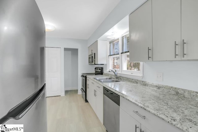 kitchen with stainless steel appliances, light stone counters, a sink, and white cabinetry