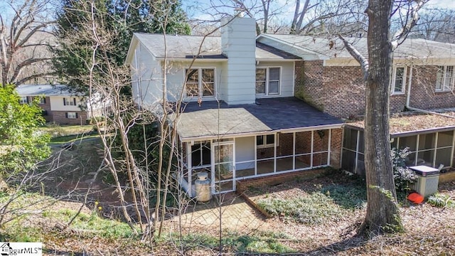 rear view of house featuring a sunroom, roof with shingles, and brick siding