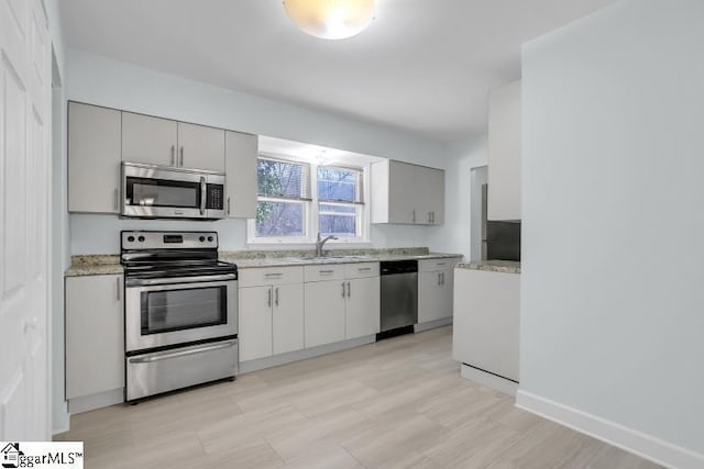 kitchen featuring baseboards, light stone counters, stainless steel appliances, and a sink