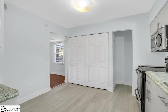 kitchen with black electric range, stainless steel microwave, light wood-style floors, white cabinets, and baseboards