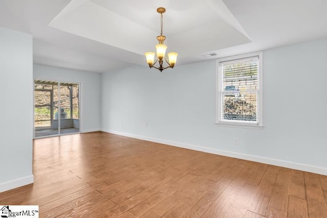 empty room featuring wood finished floors, a raised ceiling, and baseboards