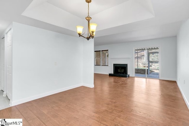 unfurnished living room with a raised ceiling, a fireplace with raised hearth, and light wood-style flooring