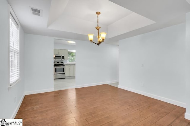 unfurnished dining area with a raised ceiling, visible vents, an inviting chandelier, light wood-style floors, and baseboards