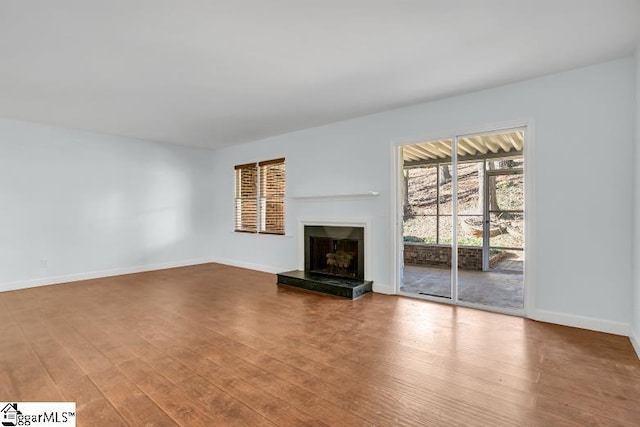 unfurnished living room with baseboards, a fireplace with raised hearth, and wood finished floors