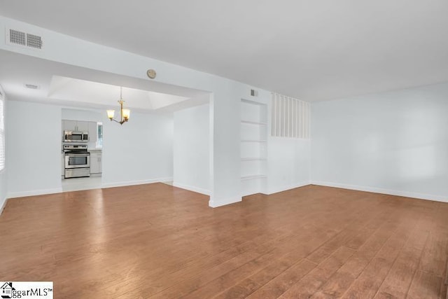 spare room with a notable chandelier, visible vents, built in features, light wood finished floors, and a tray ceiling